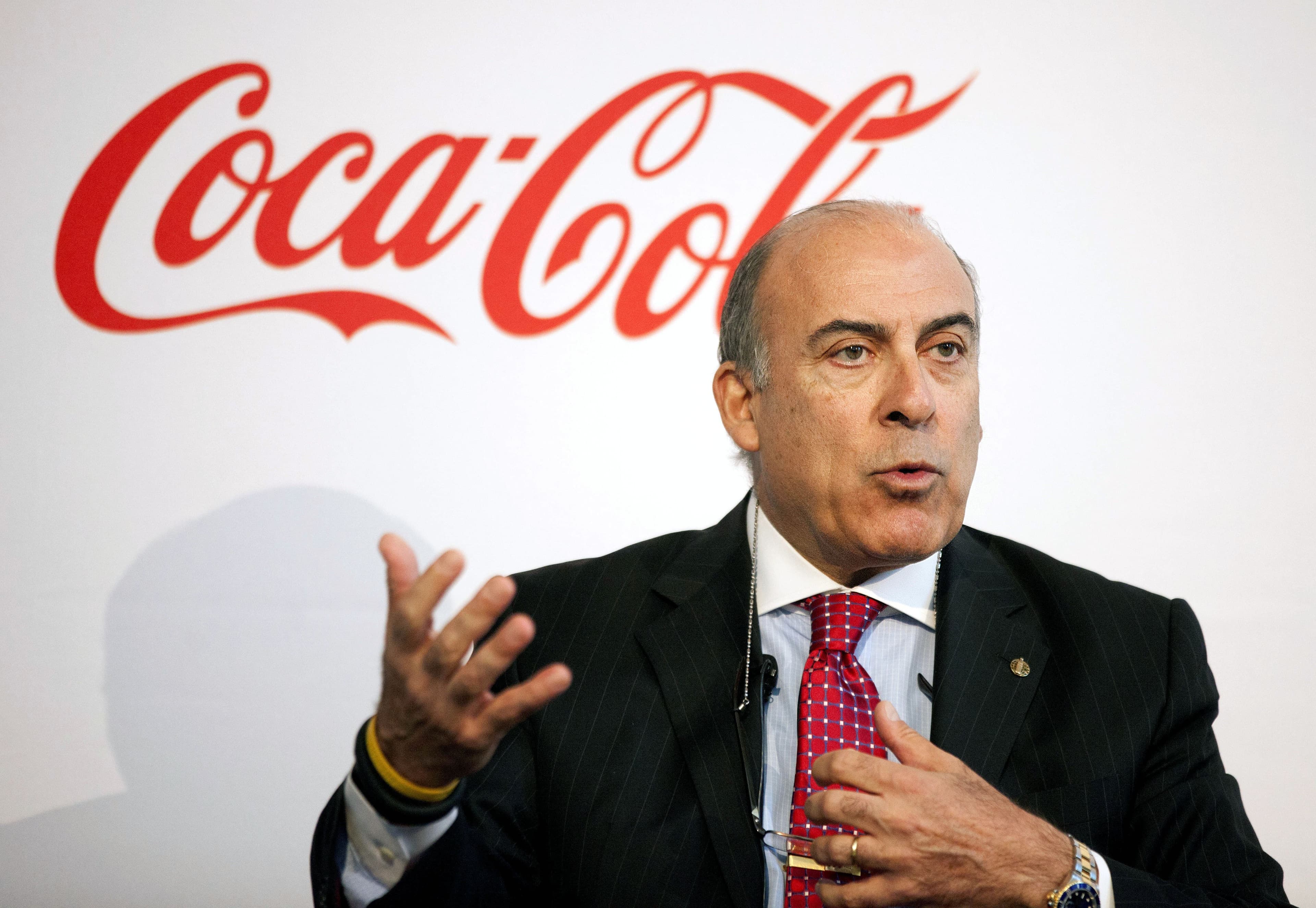 Coca-Cola CEO Muhtar Kent speaking in front of the Coca-Cola logo.