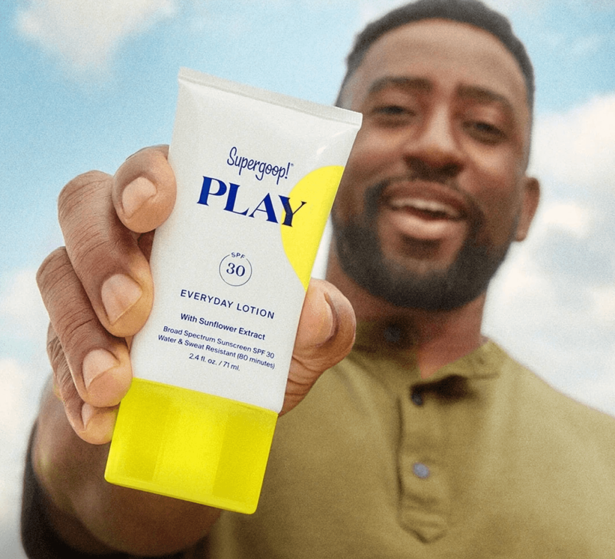 A Supergoop Play Everyday Lotion sunscreen being held up against a bright sky.